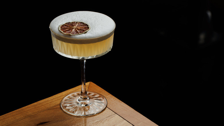 A dried citrus peel floats on the foam of a cocktail