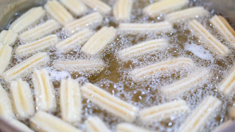 Churros frying in a pan of oil.