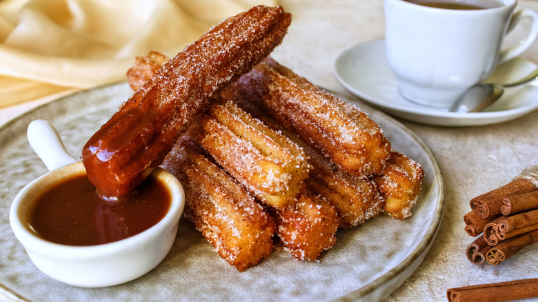 A plate of fried sugared churros with a chocolate dipping sauce.