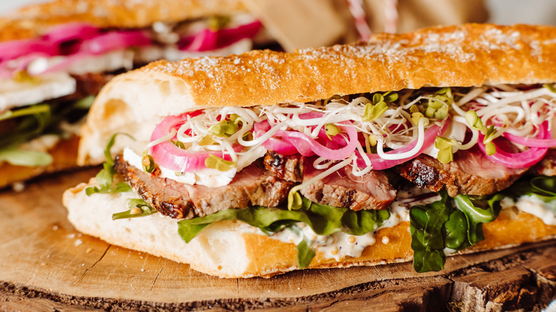 Close up of a roast beef sandwich on a sub with various toppings, all on a wooden table.