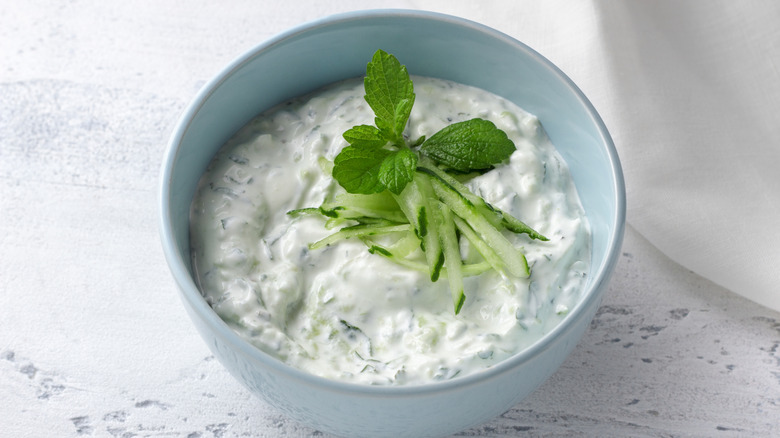 Fresh traditional Greek tzatziki with yogurt, cucumber and mint in a light blue ceramic bowl placed on light surface.