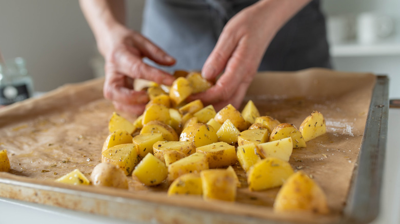 Hands arranging raw, seasoned potatoes on parchment paper-lined sheet pan