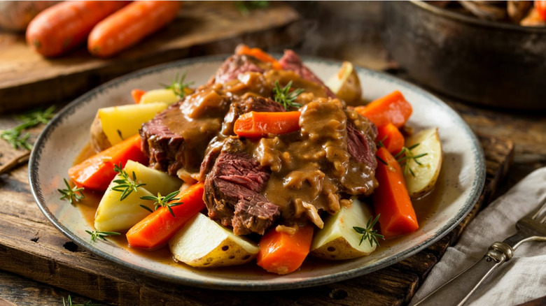 Plate with sliced pot roast, gravy, carrots, potatoes, thyme