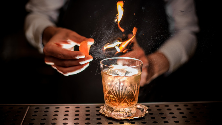 A bartender lights an orange peel aflame for a cocktail