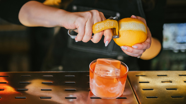 A bartender slices a citrus peel for a cocktail
