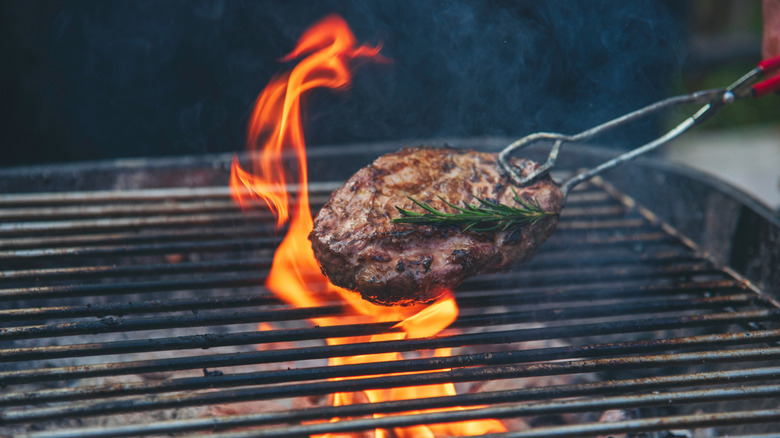 Someone cooking steak on a charcoal grill