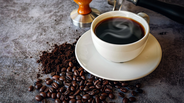 coffee in a white cup next to scattered coffee beans