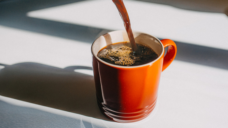 coffee being poured into a brown mug