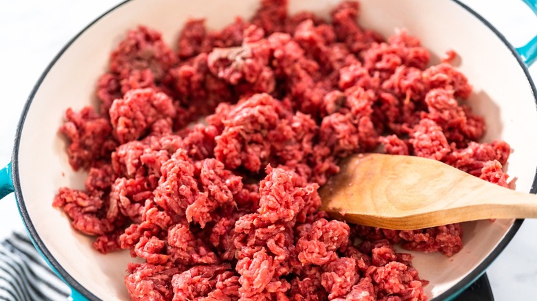 Raw ground beef in skillet with wooden spoon