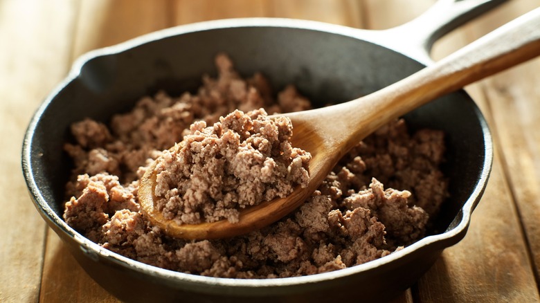 Browned ground beef in skillet with wood spoon