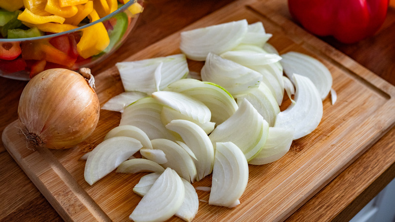 Halved onion slices on a wooden cutting board next to a whole yellow onion