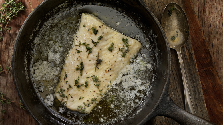A fish filet poached in butter and herbs in a cast iron pan