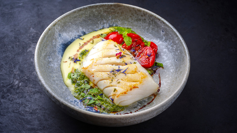 White fish filet plated with creamy sauce, roasted tomato and fresh herbs
