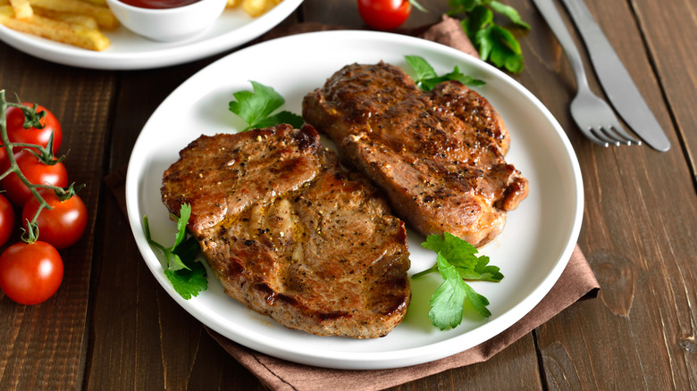 Cooked pork steaks on a white plate with a cilantro garnish