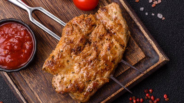 A grilled pork steak on a fork with a side of barbecue sauce