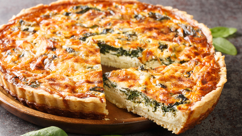 A whole quiche with a slice cut out and turned to the side on a platter.