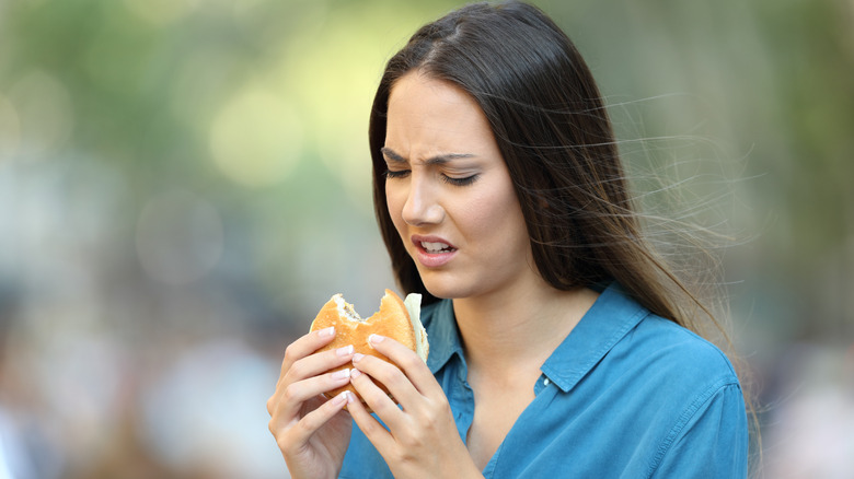 A person biting into a burger with a disgusting taste in their mouth.