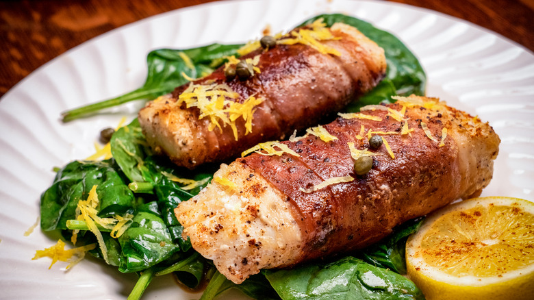 Cooked pieces of cod wrapped in prosciutto and served with spinach and lemon zest