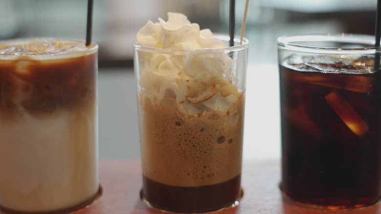 Three miniature glasses of cold brew sit in a row with straws in them.