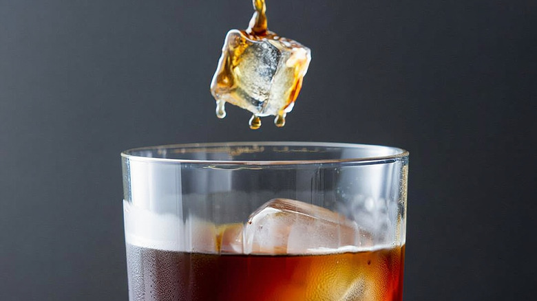 An ice cube is being dropped into a glass of iced coffee.