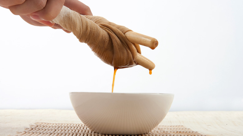 Hands strain ingredients through a cloth into a white bowl to make simple syrup.