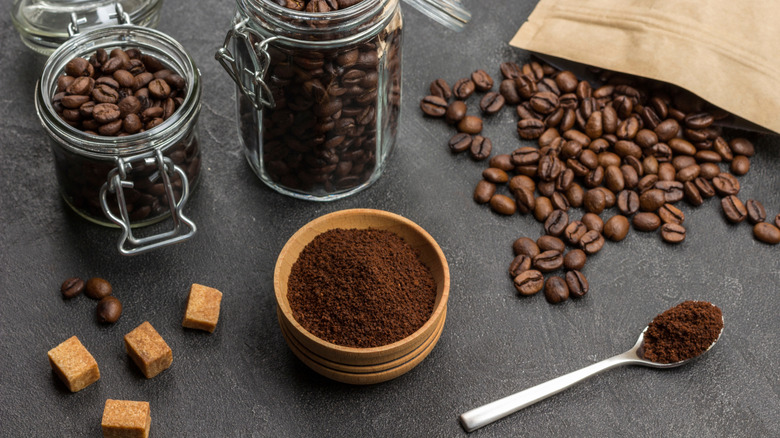 A wooden bowl of coffee grounds with two mason jars full of coffee beans on a table.