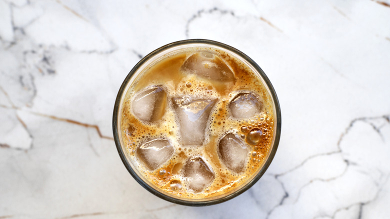 An overhead view of a glass of iced coffee, resting on a marble counter.