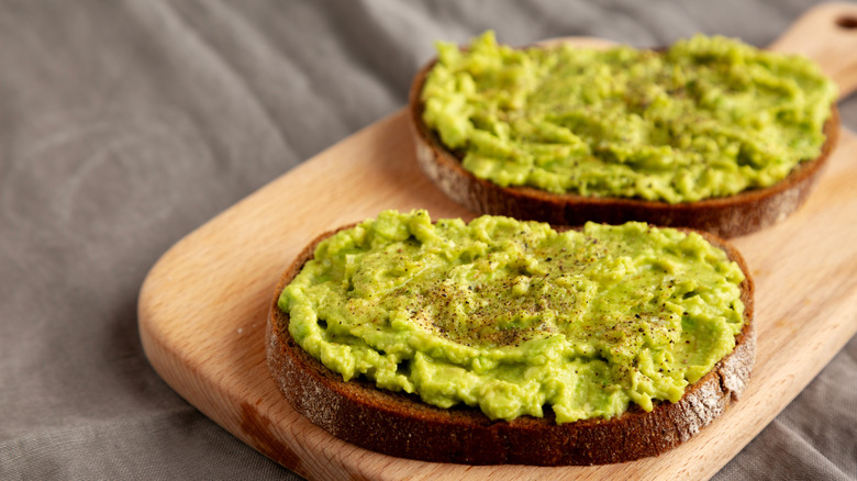 Two slices of avocado toast on top of a wooden board