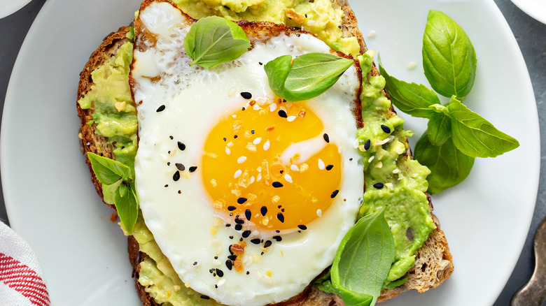 A close-up image of avocado toast with a fried egg and microgreens on top