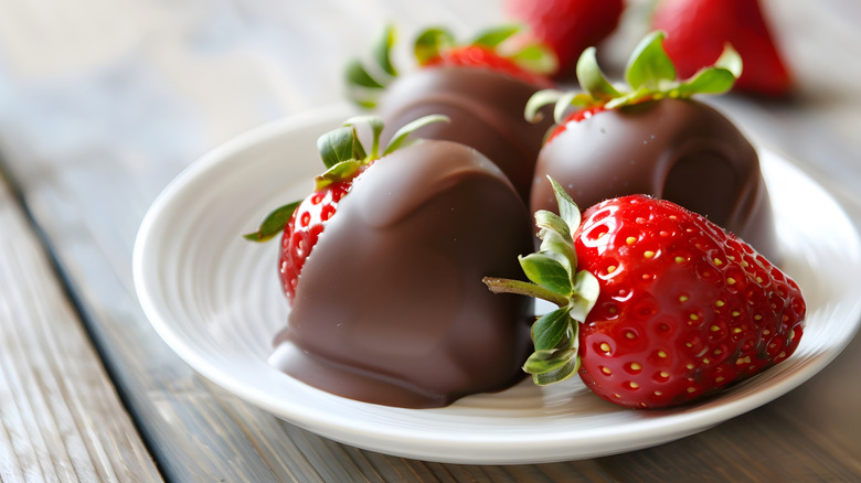 Milk chocolate covered strawberries and one plain strawberry on a white plate on a wooden table