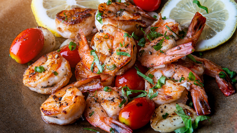 Close up of grilled shrimp on a plate with grape tomatoes, a slice of lemon and lime, and sprinkled green herbs