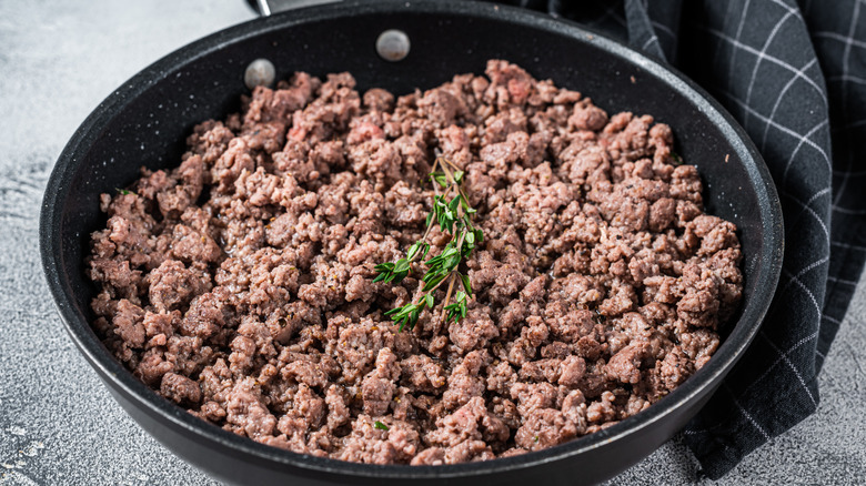 Ground beef browned in a pan with a sprig of rosemary on top