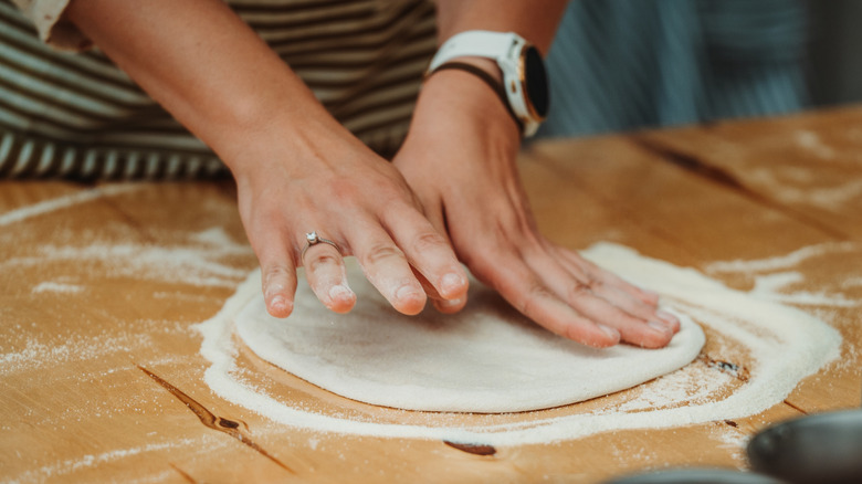 Hands pressing out a round of pizza dough