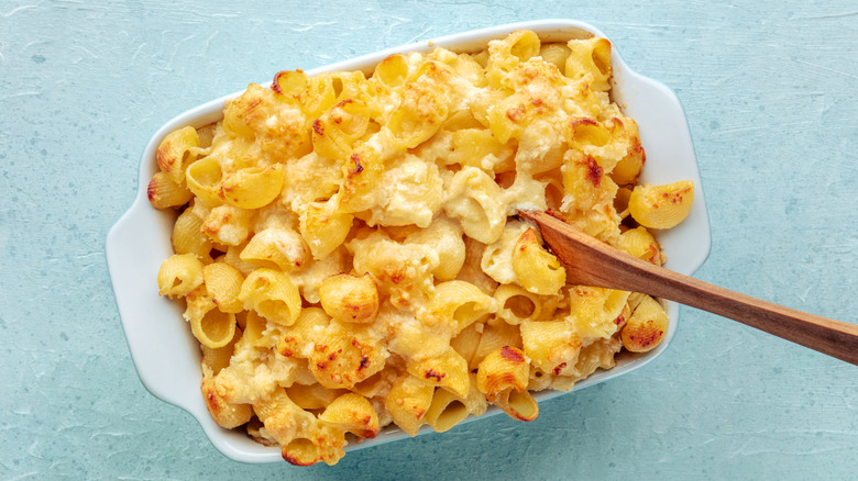 Macaroni and cheese in a white pan with a wooden utensil handle sticking out