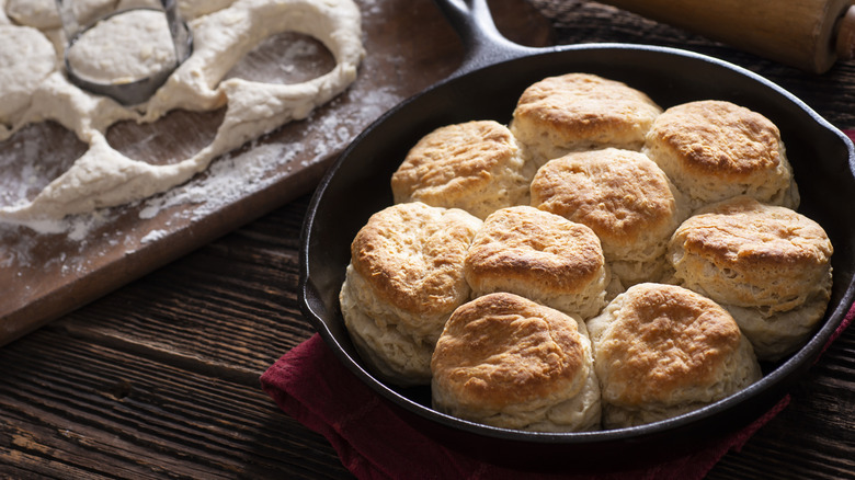 Biscuits in cast iron skillet alongside biscuit dough and cutting board
