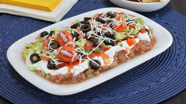 Seven layer dip in an oblong plate decorated with plastic footballs