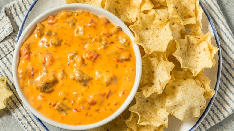 Queso dip with meat and vegetables in white bowl next to tortilla chips