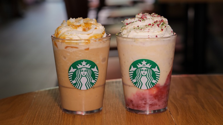 Two Starbuck's blended Frappuccinos on a wooden table with seating area blurred in the background.