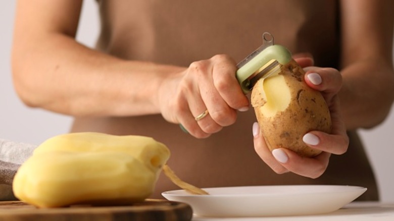 Person peeling potatoes over white plate