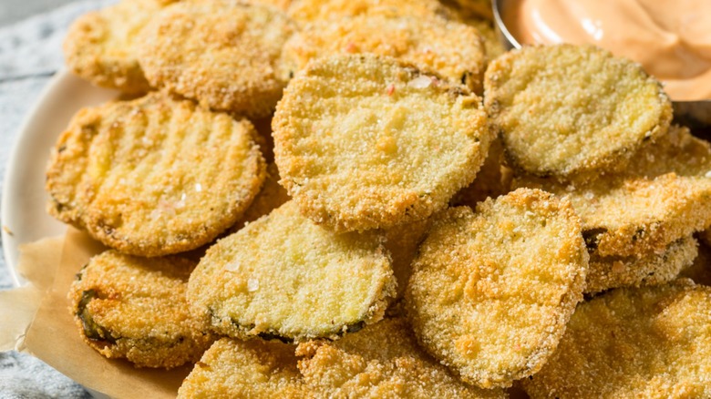 A close-up of fried pickle chips on a plate with sauce in next to it