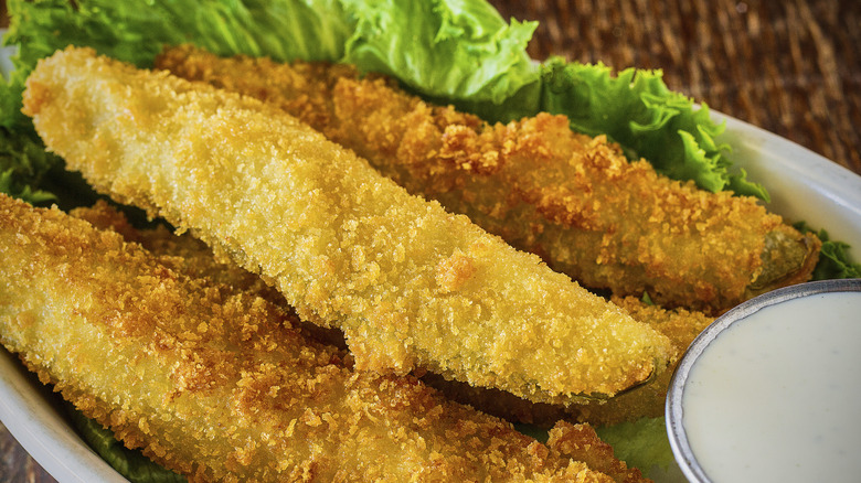 Fried pickle spears on a bed of lettuce beside a cup of ranch dipping sauce