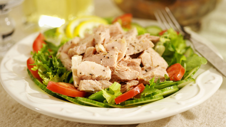 Tuna salad with greens, cucumber, and tomato on a white plate