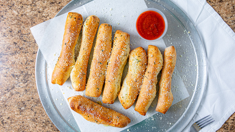 Soft breadsticks with marinara sauce on a metal tray