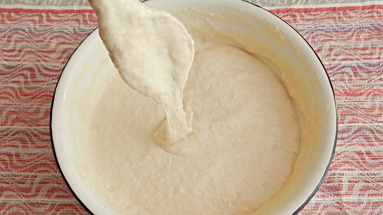 Pancake batter in white bowl with spoon dripping batter
