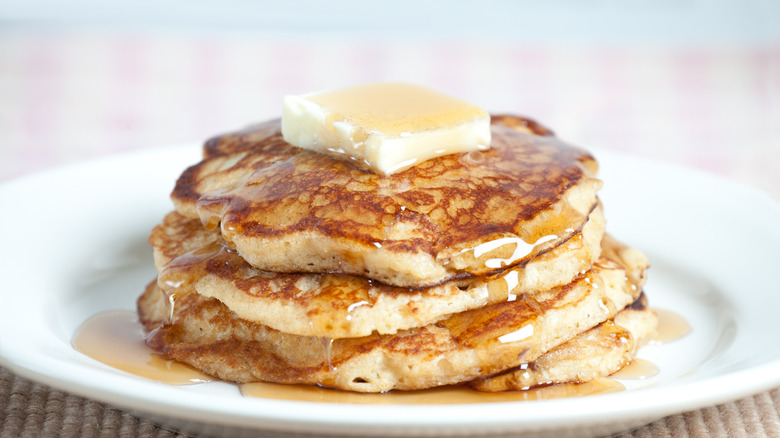 A fluffy stack of whole wheat pancakes on a plate with butter and syrup.