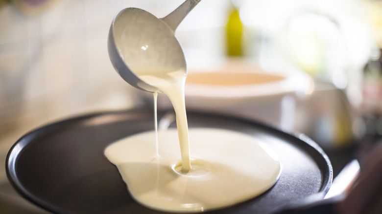 Pancake batter pours out of a ladle onto a hot griddle