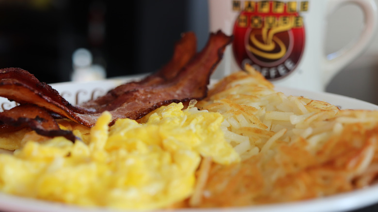 A closeup of a plate of scrambled eggs, hash browns, and bacon at a Waffle House restaurant