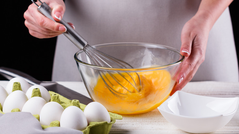 Hands whisking scrambled eggs in glass bowl