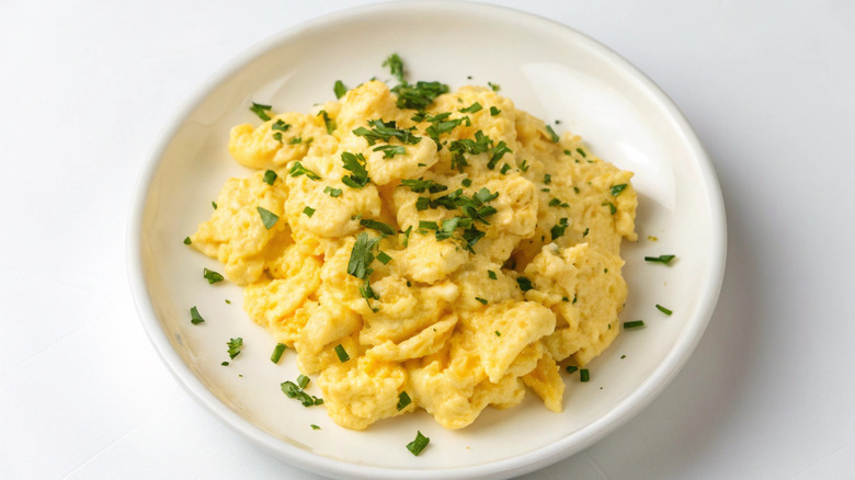 Fluffy scrambled eggs with chopped parsley on white plate