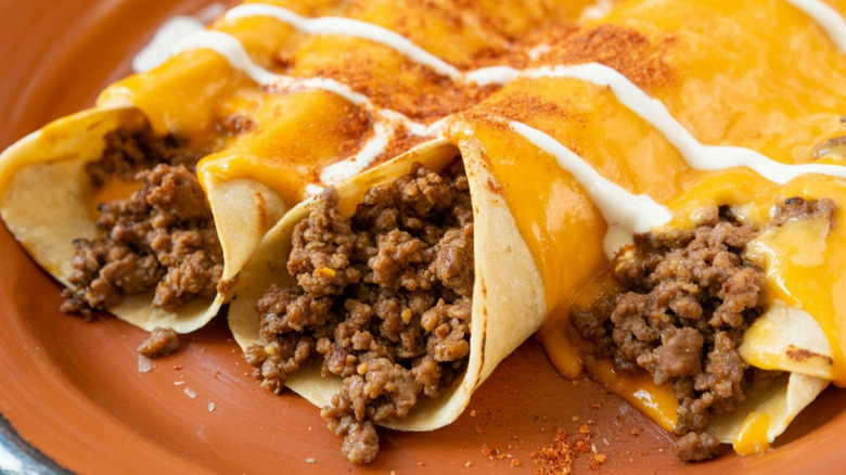 Beef enchiladas covered in cheese and sour cream on a clay plate.